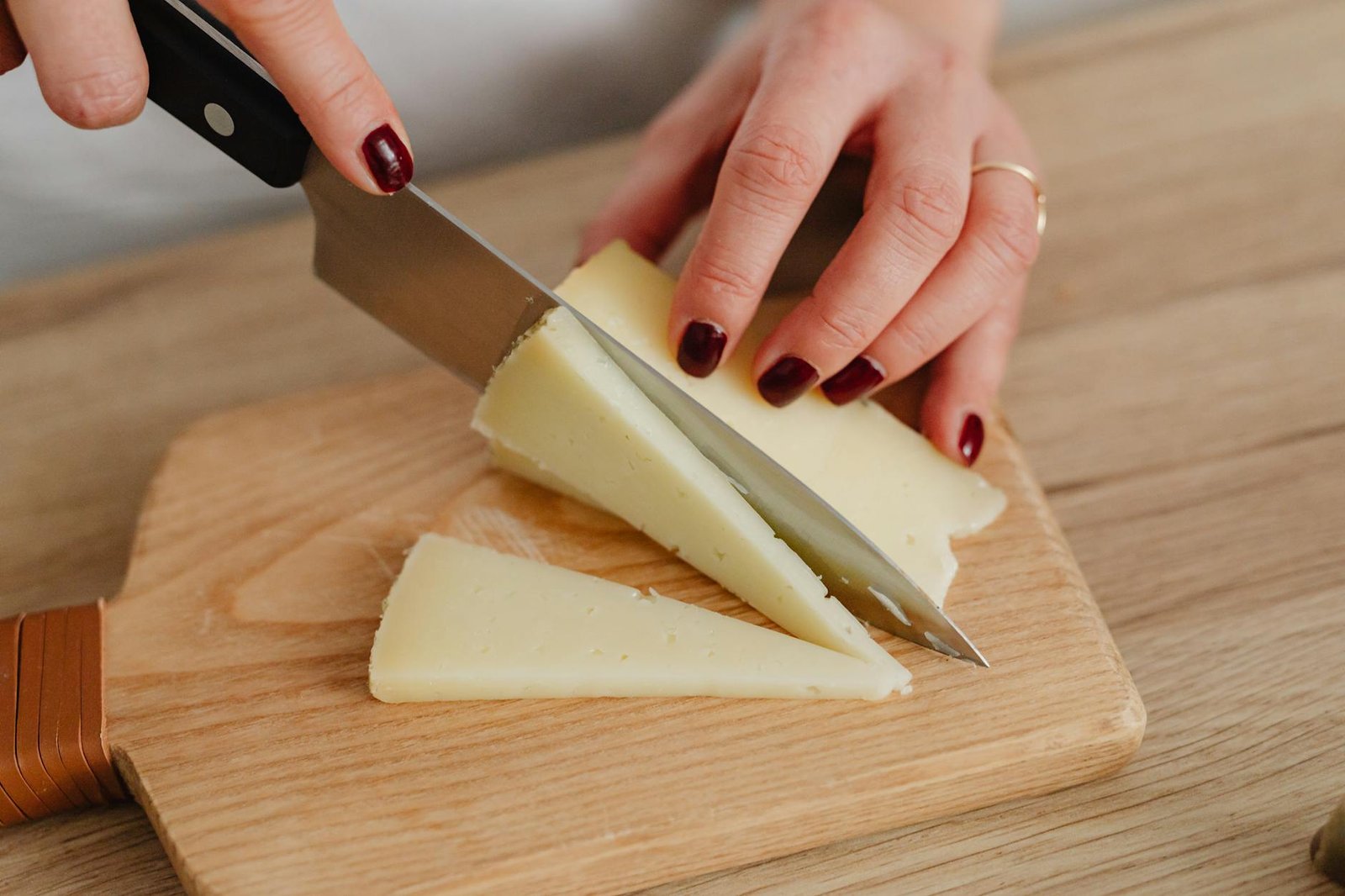 hands of a person slicing cheese on brown wooden chopping board