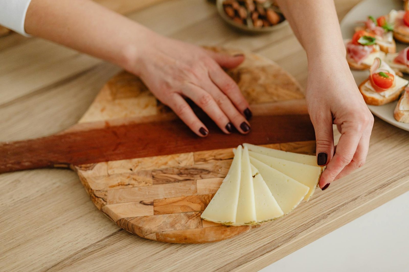 a person arranging sliced cheese on the wooden board