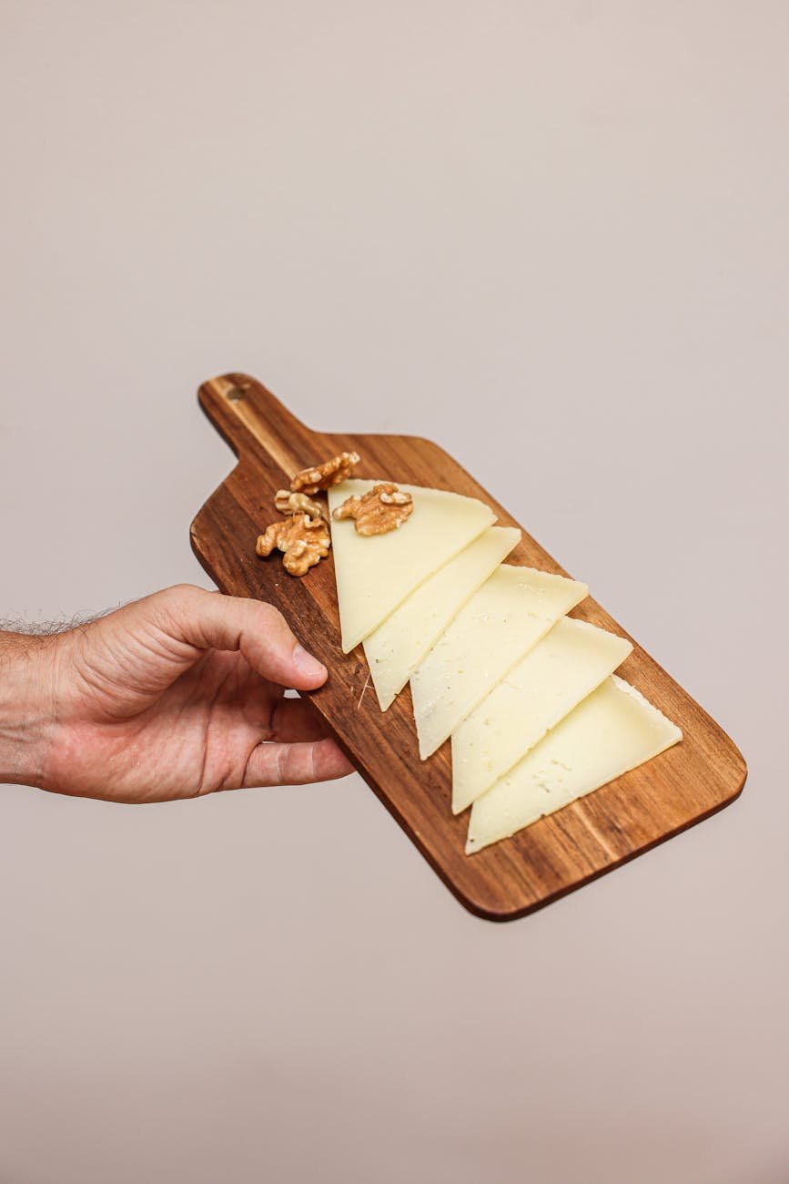 a hand holding a wooden chopping board with cheese slices